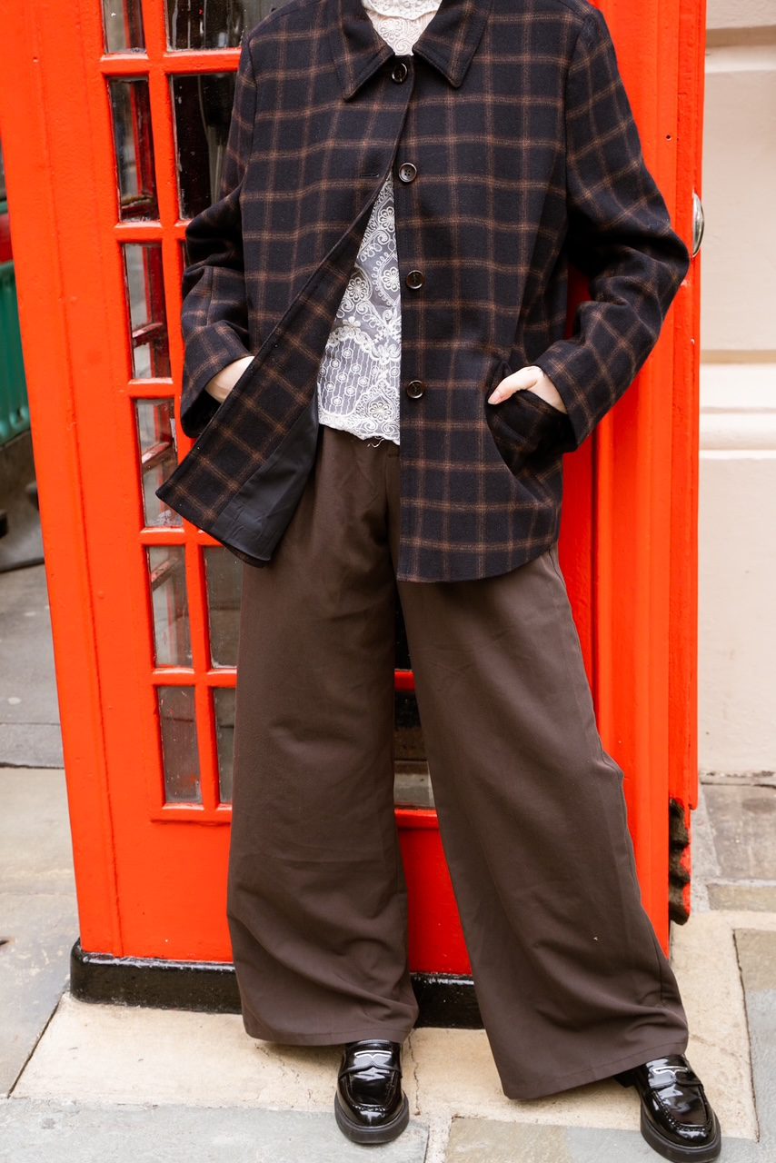 Plaid overshirt jacket over a lace top with wide-leg brown trousers against a red phone box